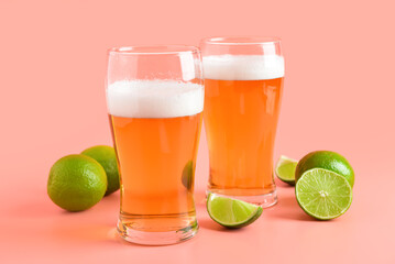 Glasses of cold beer with lime on pink background