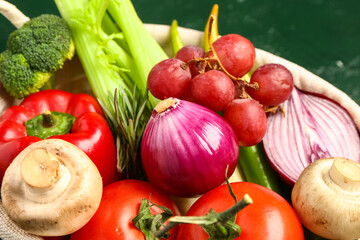 Basket with fresh ripe vegetables on green background, closeup