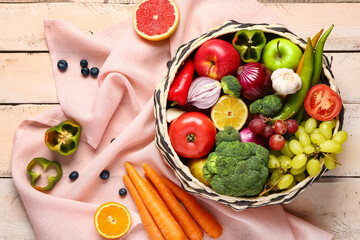 Wicker bowl with different fresh fruits and vegetables on white wooden background