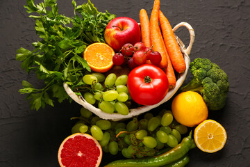 Wicker basket with different fresh fruits and vegetables on black background