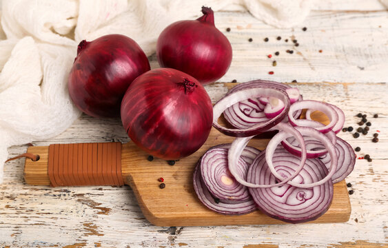 Board with slices of fresh red onion and peppercorn on white wooden background
