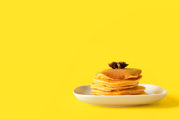 Plate with tasty pumpkin pancakes and star anise on yellow background