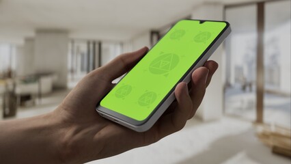 GREEN SCREEN CHROMA KEY A hand holding a smartphone with a green screen inside a renovated apartment