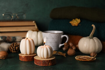 Beautiful autumn composition with candles, pumpkins and cup of tea on dark green background