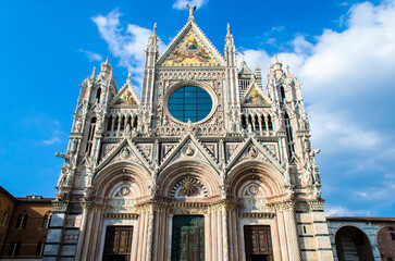 La facciata del duomo di Siena in una giornata estiva con il cielo azzurro e qualche nuvola