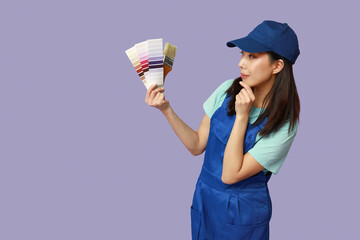 Female Asian thoughtful painter with brush and paint color palettes on purple background