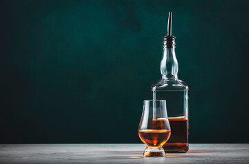 Single malt scotch whisky in glencairn glass with bottle on dark green background