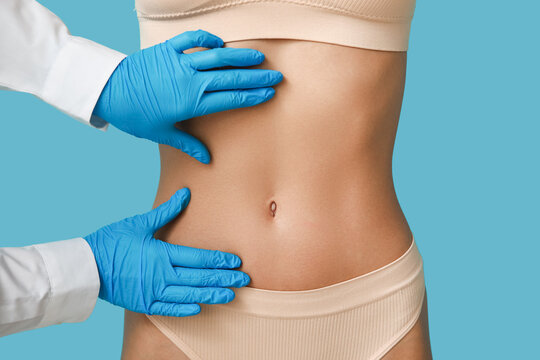 Young woman with flat belly and plastic surgeon on blue background, closeup
