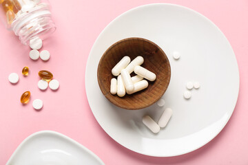 Plate, wooden bowl and bottle with different pills on pink background