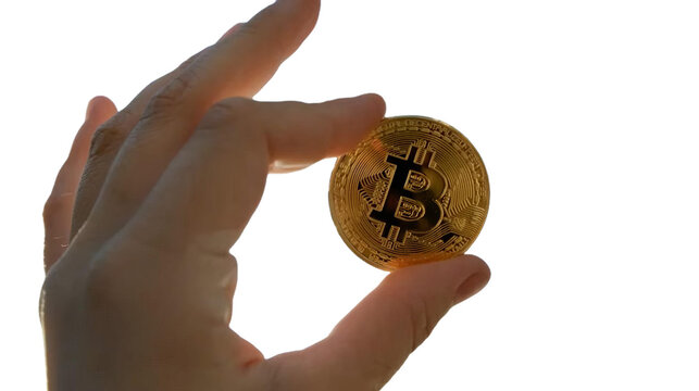 The image shows a close-up of a hand holding a physical representation of Bitcoin. The Bitcoin symbol "₿" in the center. You can place this background-removed PNG file wherever you like.
