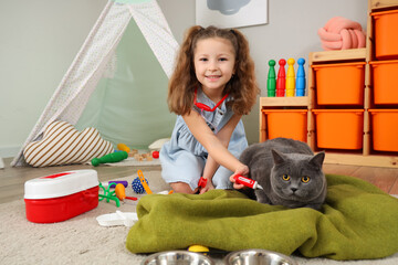 Cute little girl with British cat, thermometer and first aid kit at home