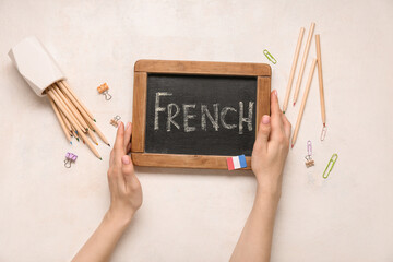 Female hands, chalkboard with word FRENCH and stationery on light background