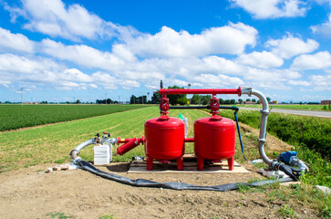 Due pompe rosse per l'irrigazione dei campi in una giornata estiva con un cielo pieno di piccole nuvole bianche