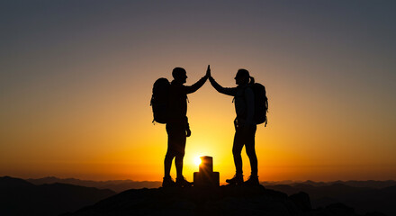 Fototapeta premium Hikers celebrating a triumphant sunrise summit high-five against a fiery orange and yellow sky silhouette