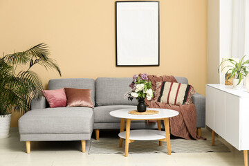 Beautiful living room with bouquet of lilacs branches on coffee table, cozy sofa and cushions