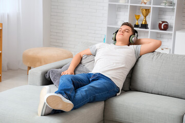 Teenage boy in headphones resting on sofa at home