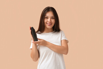 Beautiful young happy woman with hair spray on beige background