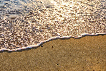 Close-up of golden beach sand at sunset with wave foam covering half of it