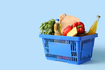 Blue shopping basket full of different fresh products and bottle of oil on blue background