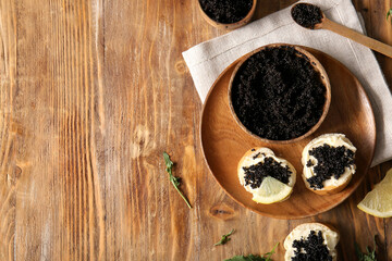 Bowl and baguette slices with delicious black caviar on wooden background