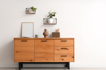 Chest of drawers, picture frame and shelves with houseplants on white wall in living room