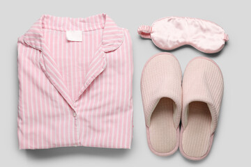 Striped pajamas with slippers and sleeping mask on light background