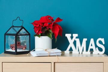 Christmas plant poinsettia with letters to Santa and decor on commode near blue wall