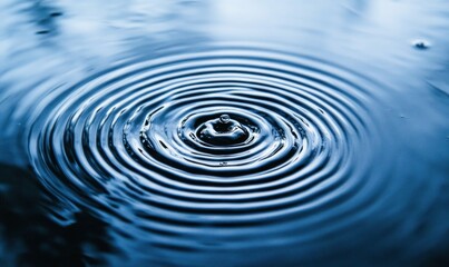 A single water droplet creates calming ripples across the dark blue water's surface in a mesmerizing concentric pattern.