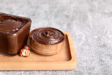 Bowls of sweet chocolate spread and hazelnuts on grey background