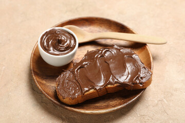 Wooden plate of bread slice with sweet chocolate spread on beige background