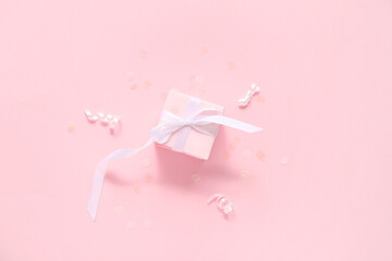 Pink gift box with serpentine and confetti on color background