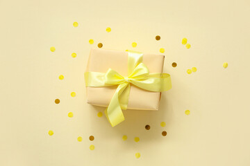 Yellow gift box and confetti on color background