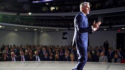 Confident businessman delivering inspiring keynote speech to large audience in modern auditorium