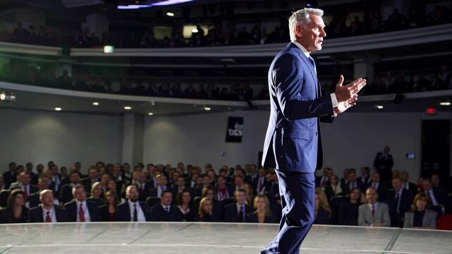 Confident businessman delivering inspiring keynote speech to large audience in modern auditorium