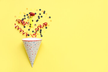 Party hat with whistle and confetti on yellow background