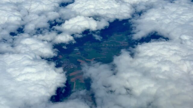 A breathtaking aerial view of a vast and lush landscape that is partially hidden by soft, fluffy white clouds