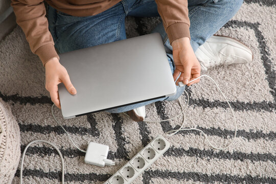 Young woman getting out charger from laptop on carpet, top view. National Day of Unplugging