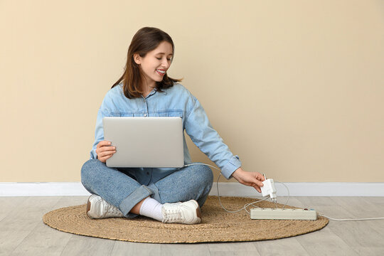 Young woman getting out laptop charger from extension cord near beige wall. National Day of Unplugging