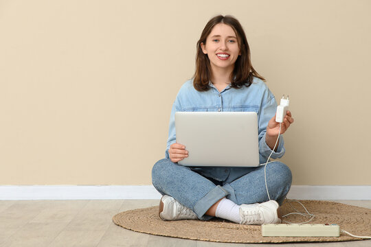 Young woman with laptop and charger sitting near beige wall. National Day of Unplugging