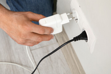 Male hand unplugging charger from socket on light wall, closeup