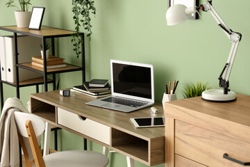 Modern workplace with blank laptop near green wall in office