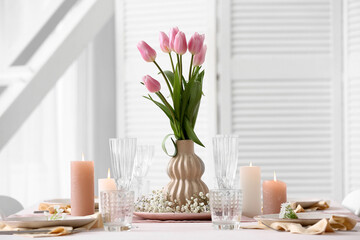 Beautiful table setting for Mother's Day celebration with tulip flowers and burning candles in dining room, closeup