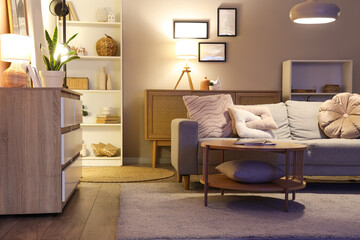 Interior of living room with sofa, shelf unit and glowing lamps in evening