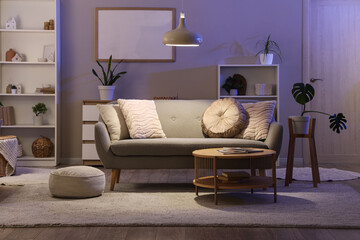 Interior of living room with grey sofa, table and glowing lamp in evening
