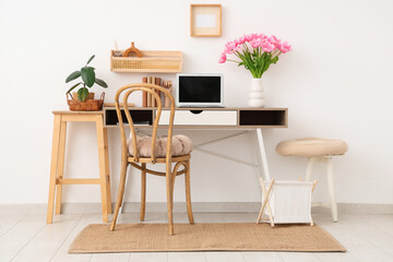 Interior of modern workplace with stools, shelves, laptop and beautiful tulip flowers in vase