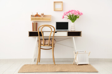 Interior of modern workplace with shelves, books, laptop and beautiful tulip flowers in vase