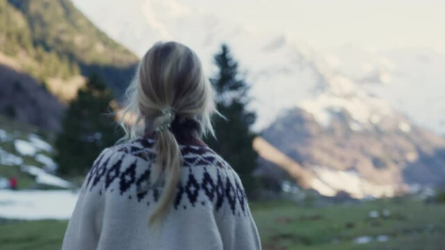 Blonde girl 7 years old walking along alpine valley, approaching traditional wooden cabin nestled beneath snow covered Pyrenees mountain peaks, embodying serene outdoor exploration and solitary