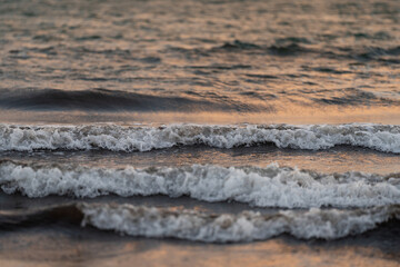 Close-up of gentle waves rolling across the surface of the sea at dusk. The soft lighting reflects...