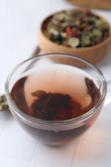 Delicious herbal tea and dry leaves on white tiled table, closeup