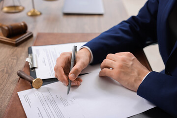 Notary signing document at wooden table in office, closeup